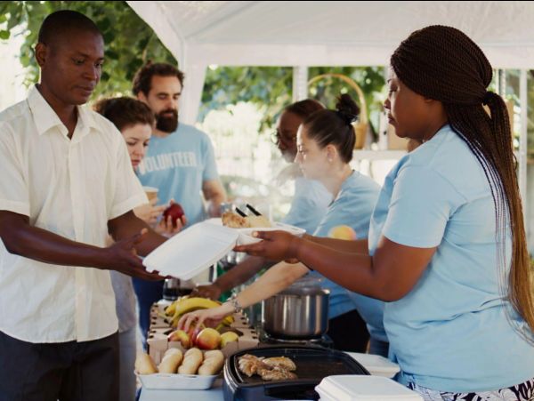 Volunteers serve food to a man at a community event.