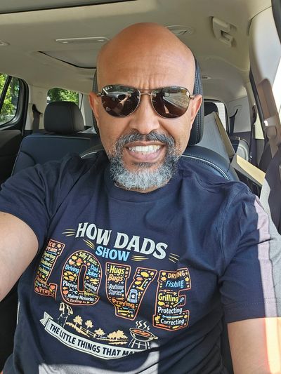 Man wearing sunglasses and a humorous dad-themed t-shirt inside a car.