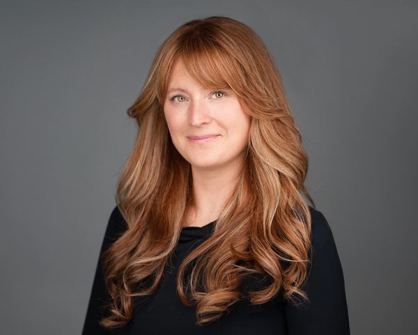 Smiling woman with long wavy red hair against a gray background.