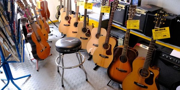 Verkaufsraum mit Akustikgitarren, Verstärkern, Noten und einem Hocker, welche zum Verkauf stehen
