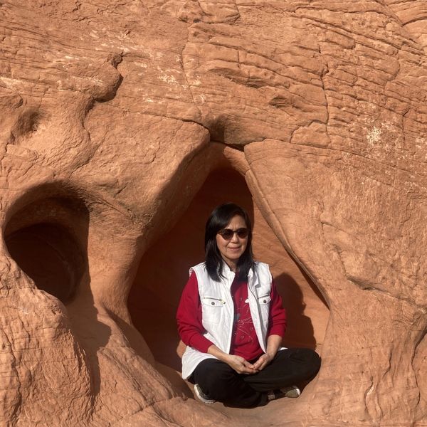 Woman sitting inside a naturally formed rock cavity, wearing sunglasses and casual clothes.
