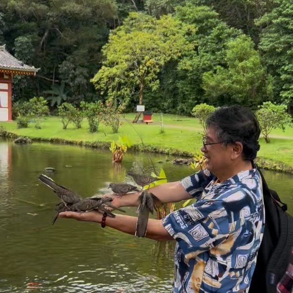 Man feeding birds by a serene pond in a lush garden.