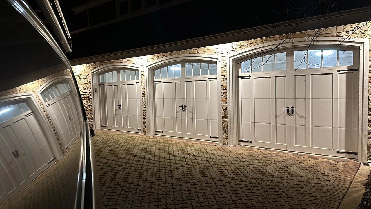 Three illuminated garage doors on a brick house at night.