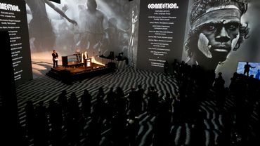 Audience watches a cultural event with large black-and-white projections and a speaker on stage.