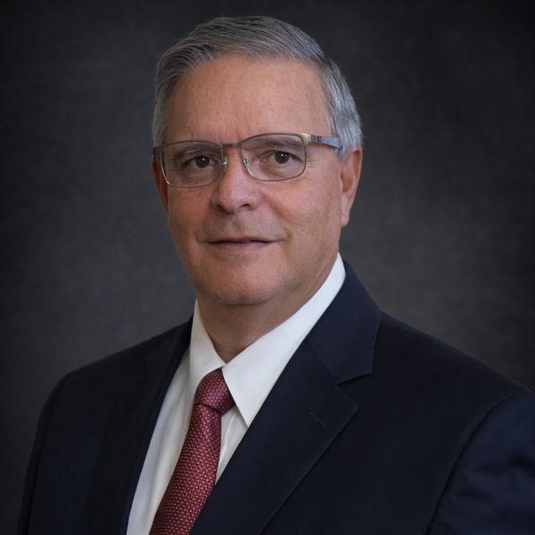Professional portrait of a mature man in a suit and tie with glasses.