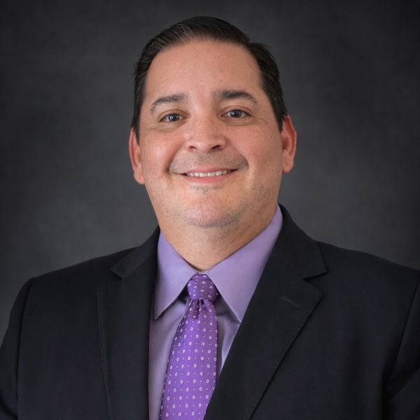 Professional man in a suit smiling against a dark background.