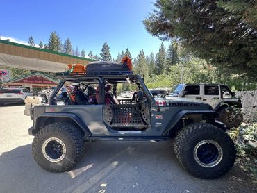 A rugged Rubicon Jeep with oversized tires and a dog wearing goggles inside.