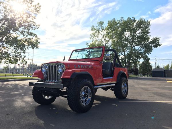 Red Jeep Laredo with large tires parked in an open lot under a sunny sky.