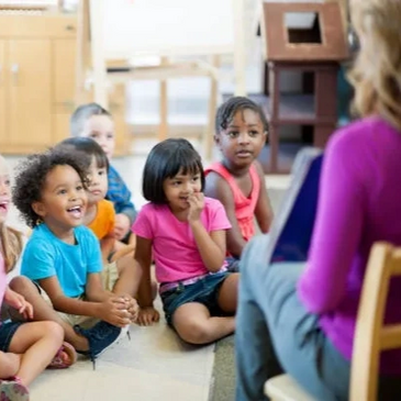 A group of young children listening attentively to a teacher during storytime.