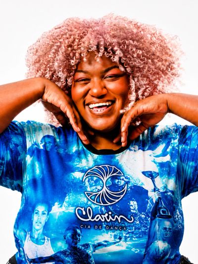 Smiling woman with curly pink hair wearing a vibrant blue shirt.