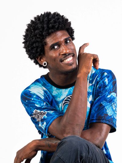 Smiling man with curly hair pointing upwards in a blue patterned shirt.
