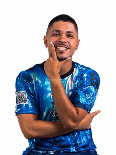 Smiling man in a blue patterned shirt poses confidently with hand on chin.