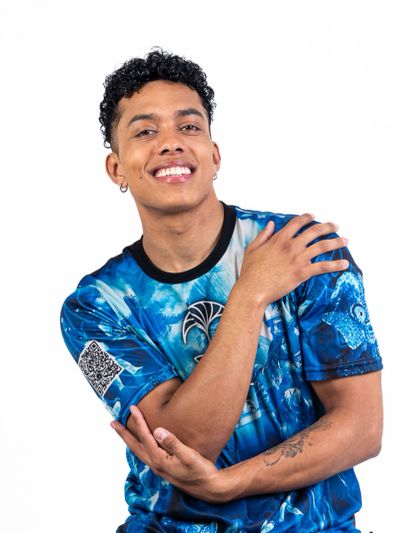 Smiling young man with curly hair in a blue graphic T-shirt posing confidently.