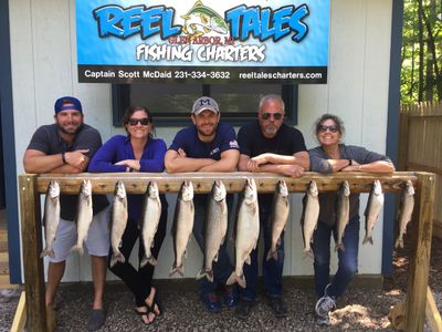 People standing in front of Reel Tales Charter Fishing board