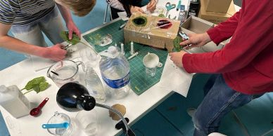 Two people working on a craft project at a cluttered table.