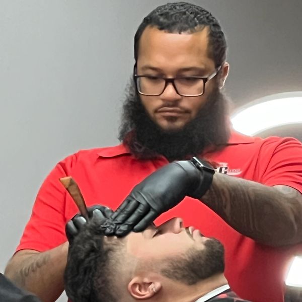 Barber wearing gloves carefully shaping a client's hairline with a straight razor.