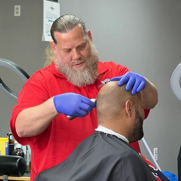Barber with a beard trimming a client's hair wearing blue gloves.