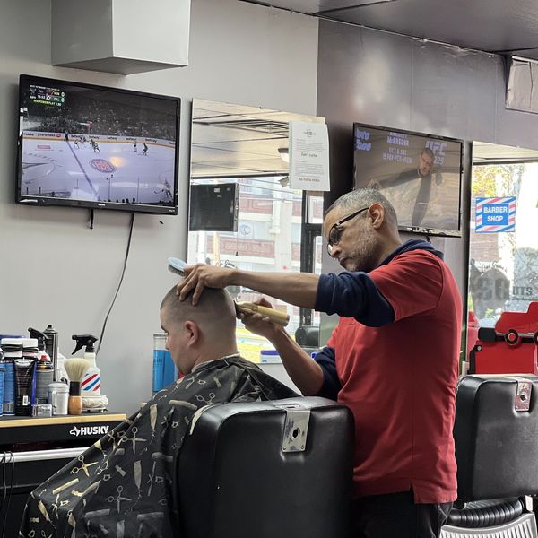 A barber giving a haircut in a shop with sports on TV.