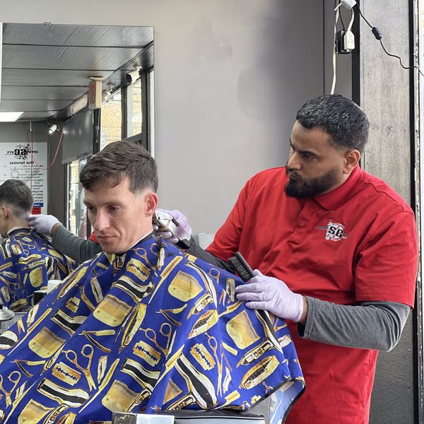Barber giving a haircut to a man in a vibrant blue cape with barber tools pattern.