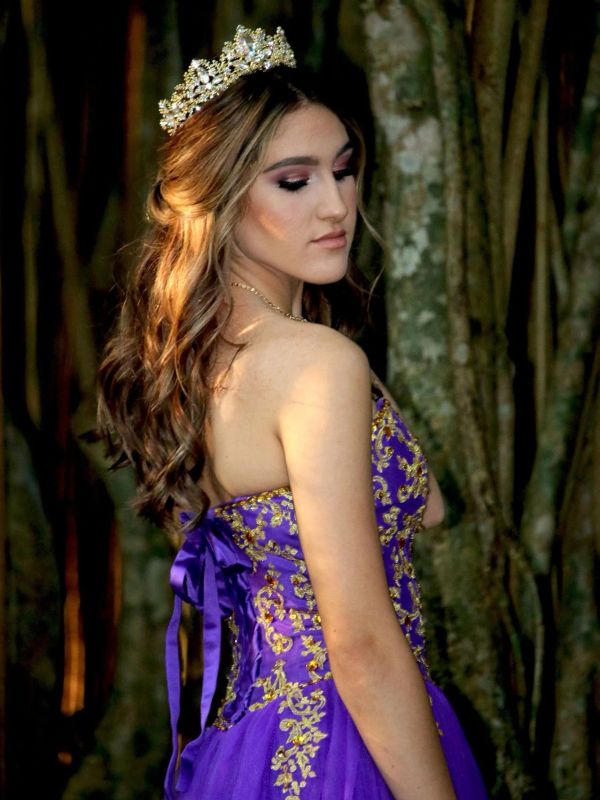 Young woman in purple dress and tiara posing outdoors.