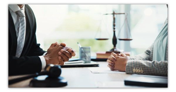 Two people in a consultation with scales of justice in background.