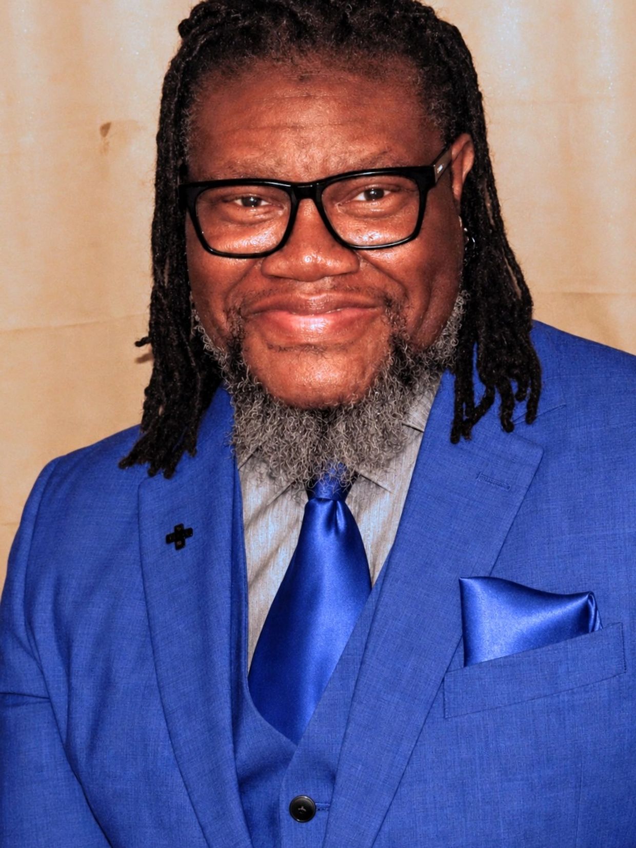 Smiling man in a vibrant blue suit and tie with glasses and a beard.