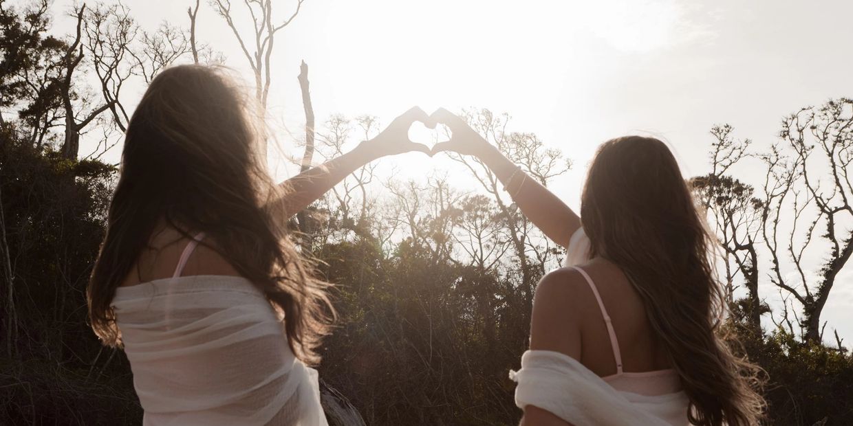 Two women making a heart shape with their hands at sunset.