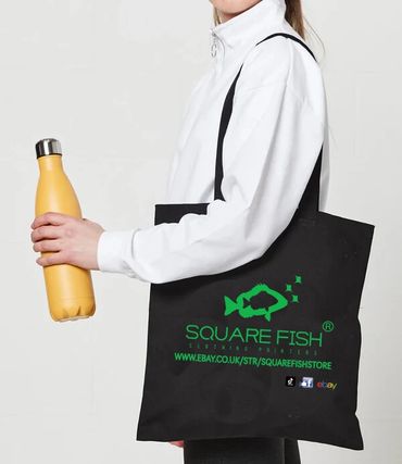 Person holding a yellow bottle and black Square Fish tote bag.