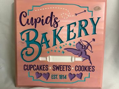 Pink sign for Cupid's Bakery with cupcakes, sweets, and cookies.