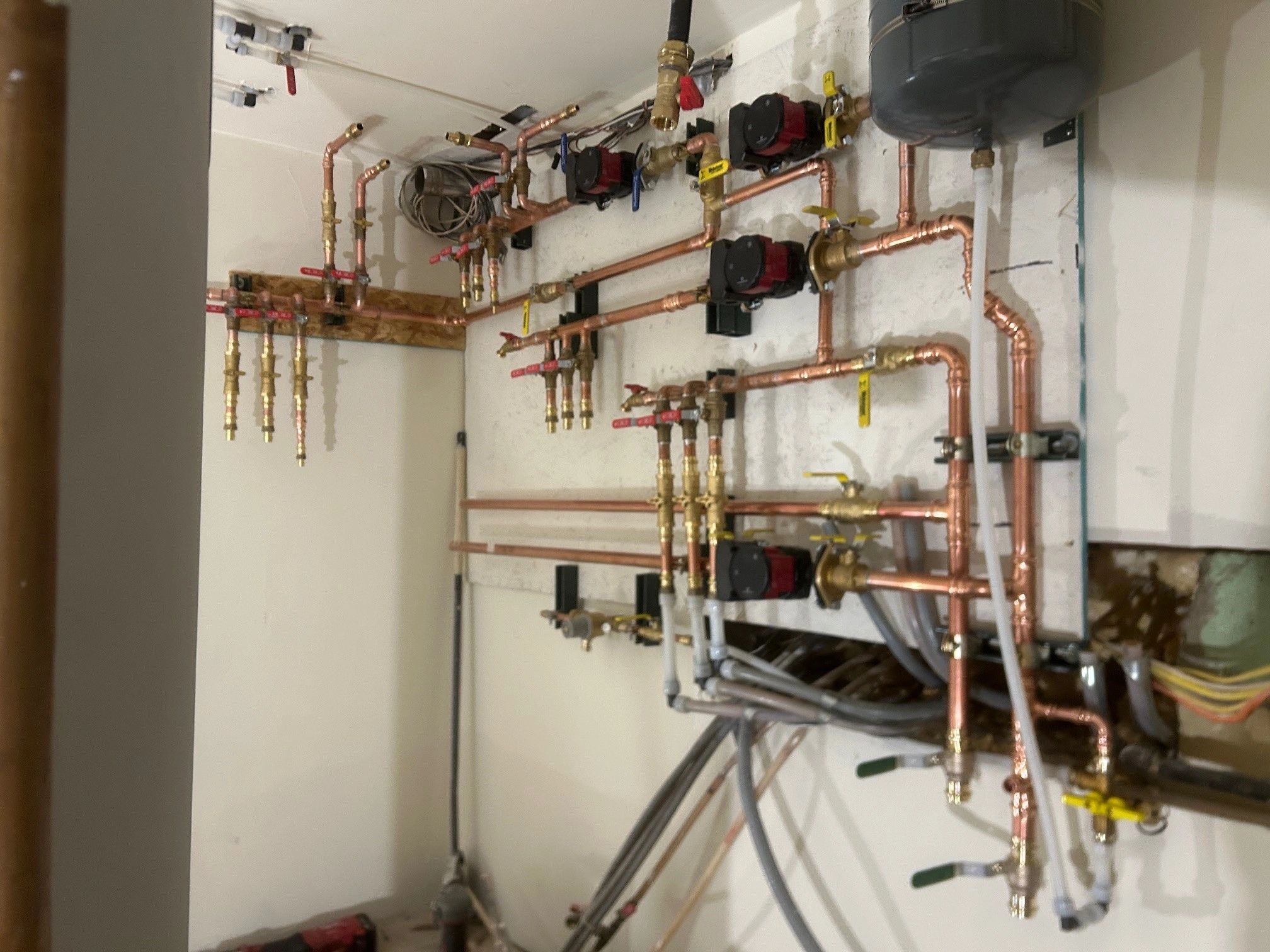Complex copper pipe system with multiple valves and pumps mounted on a wall.