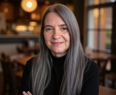 Smiling woman with long gray hair in a cozy indoor setting.