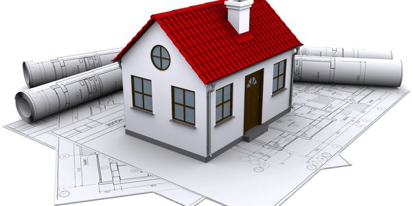 Model house with red roof on architectural blueprints and rolled plans.