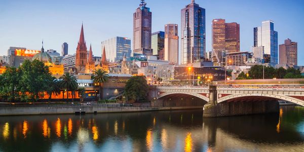 A city skyline with a river and bridge at dusk reflecting lights.