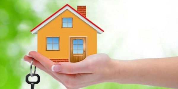 Hand holding a small model house with a key, symbolizing home ownership.