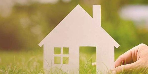 Hand holding a paper house cutout on grass.