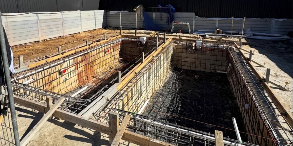 Construction site showing foundation and rebar framework for a large rectangular structure.