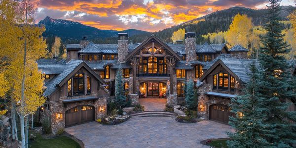Large rustic stone mansion at sunset with mountain backdrop.