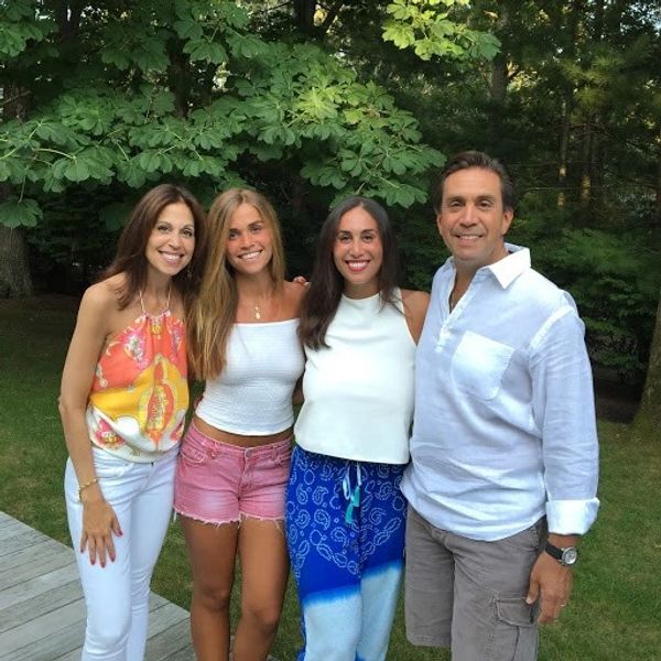 Smiling family of four posing outdoors with greenery.