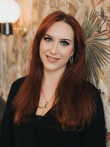Smiling woman with long red hair standing by a decorative wall.