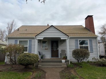 Front view of a gray house with a porch and chimney.