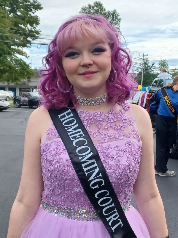 Young woman in a purple dress wearing a Homecoming Court sash.