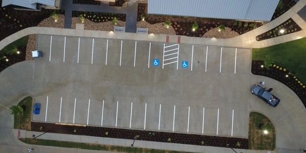 A nearly empty parking lot with two handicapped spaces and one parked car.