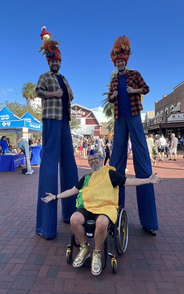 Randy in his wheelchair dressed as a taco for Hometown Halloween with stilt walkers behind him.