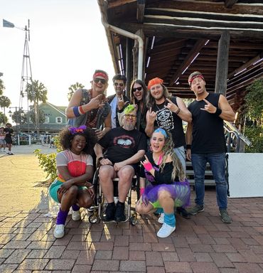 Randy posing in a wheelchair with band members of Fancy Raegan around him.