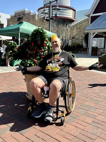Randy in his wheelchair next to a street performer dressed up as a strawberry bush.