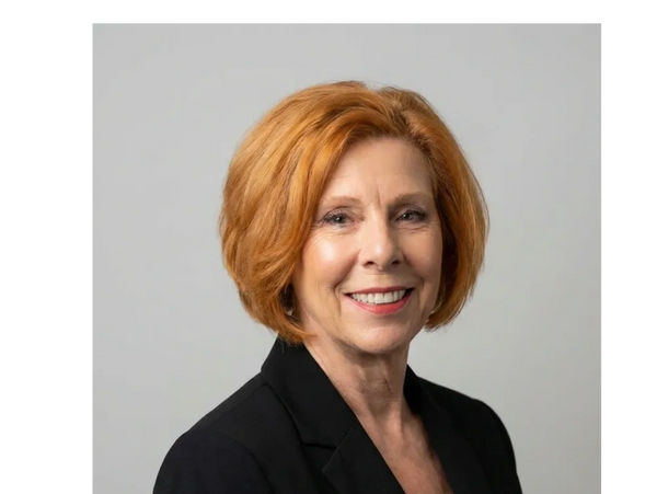 Professional portrait of a smiling woman with red hair in a black blazer.