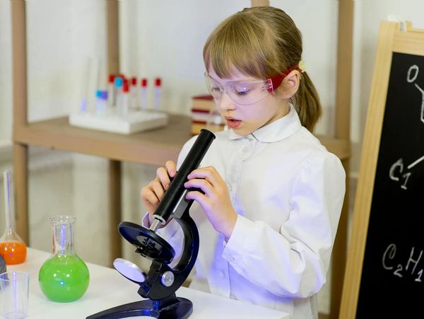 Young girl in a lab coat using a microscope in a science classroom.