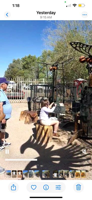 A girl operates a mechanical butterfly sculpture while an older man watches outdoors.
