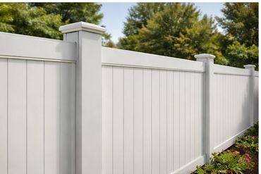 White vinyl privacy fence with greenery in the background.