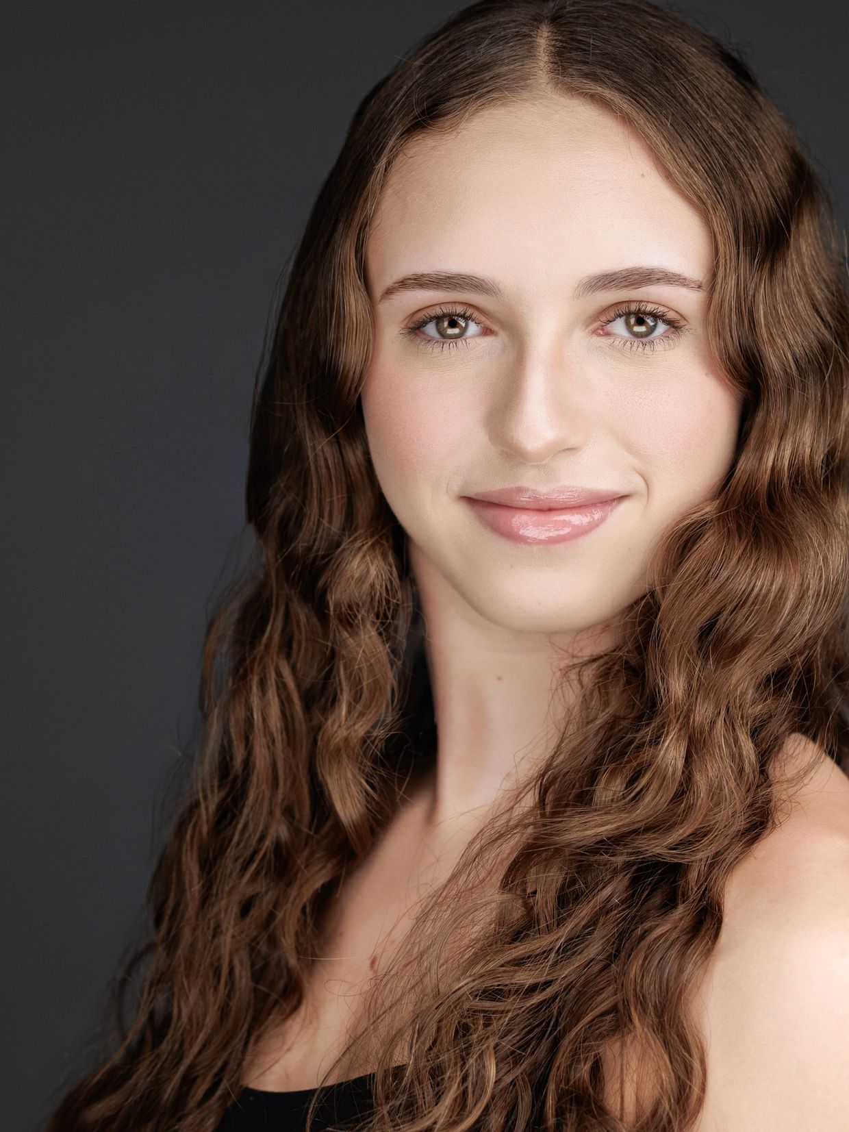 Young woman with long wavy hair smiles gently against a dark background.